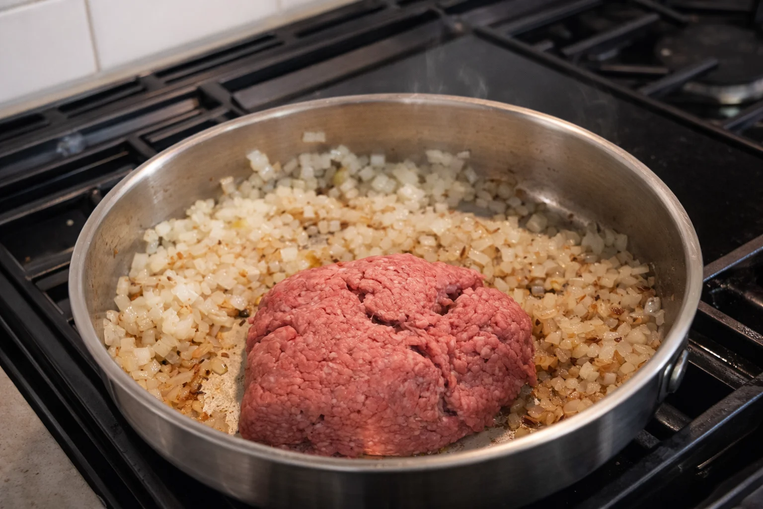 Raw ground beef added on top of sautéed onions in a stainless steel skillet