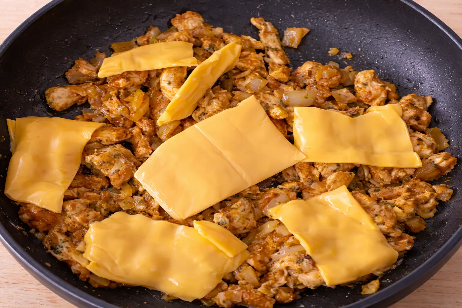 Melted cheddar cheese over seasoned chicken in a pan