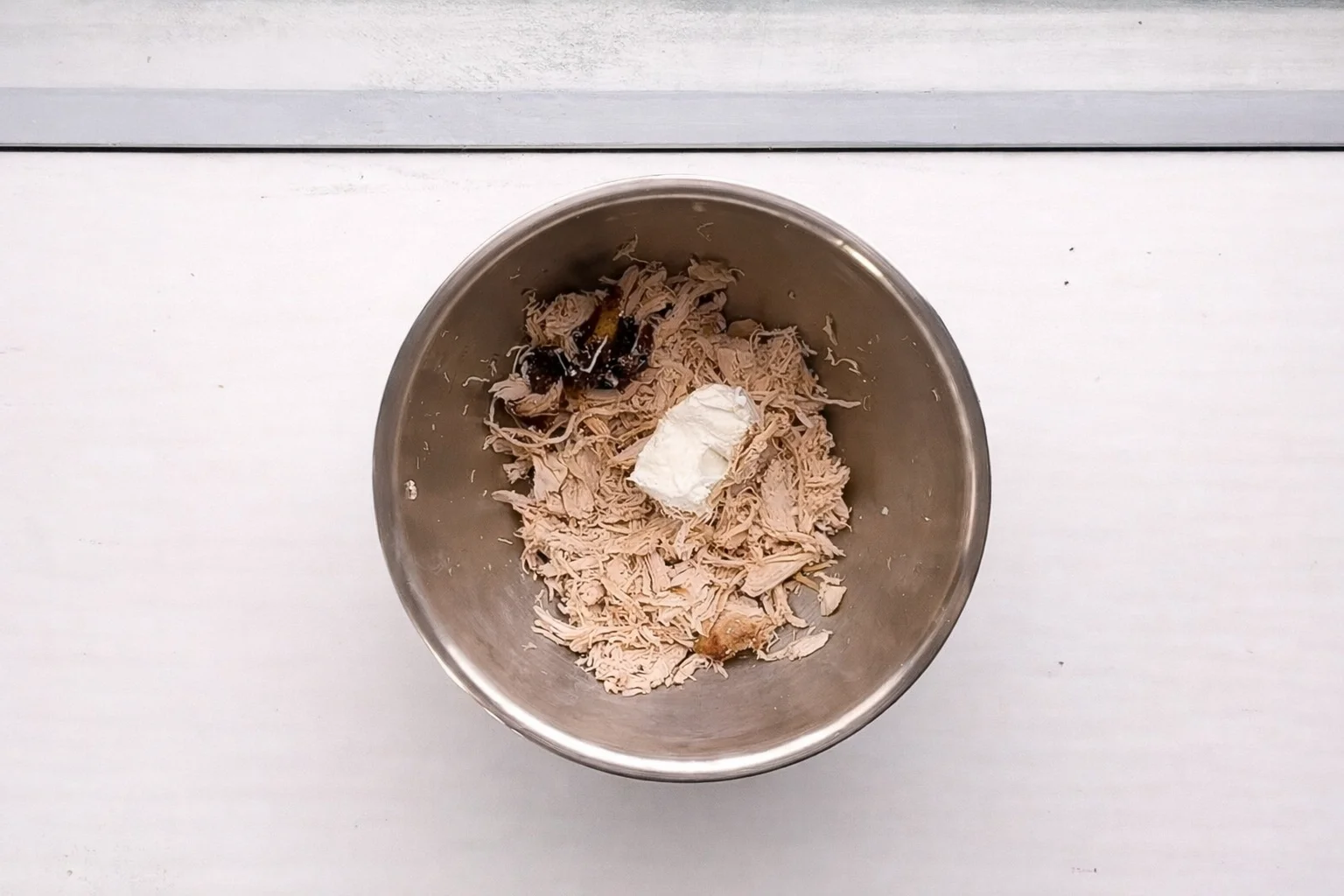 Shredded chicken with buffalo sauce and cream cheese in mixing bowl before combining
