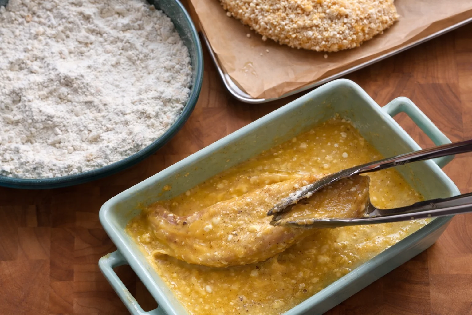 Chicken tender dipped in egg mixture as part of the breading process for garlic parmesan chicken tenders