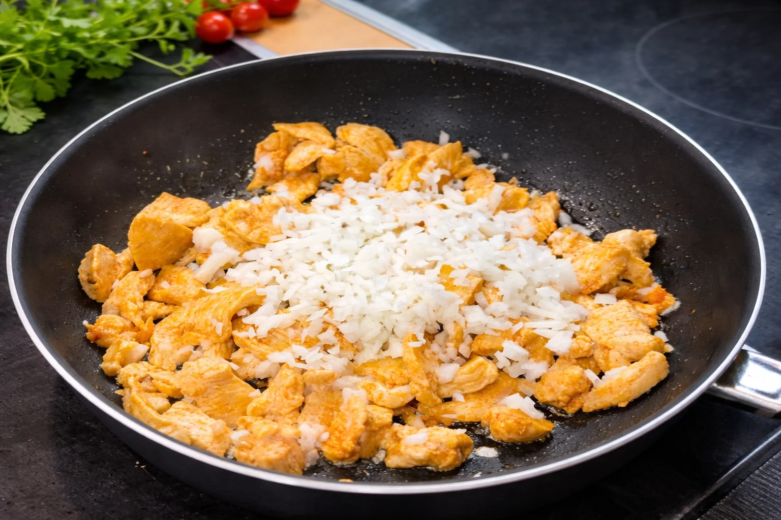 Chopped onion added to seasoned chicken in skillet