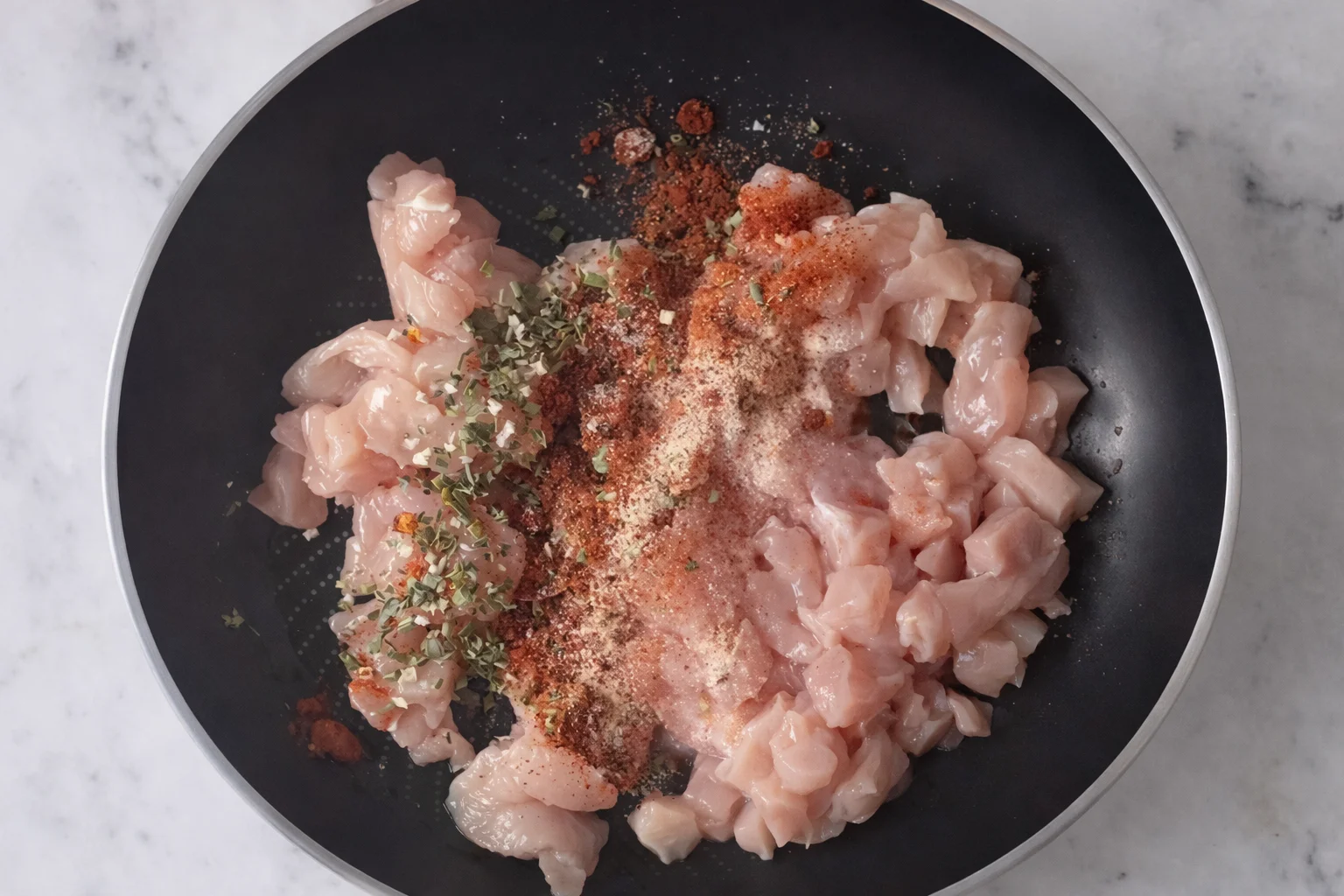 Raw diced chicken in a bowl coated with spices and dried herbs before cooking