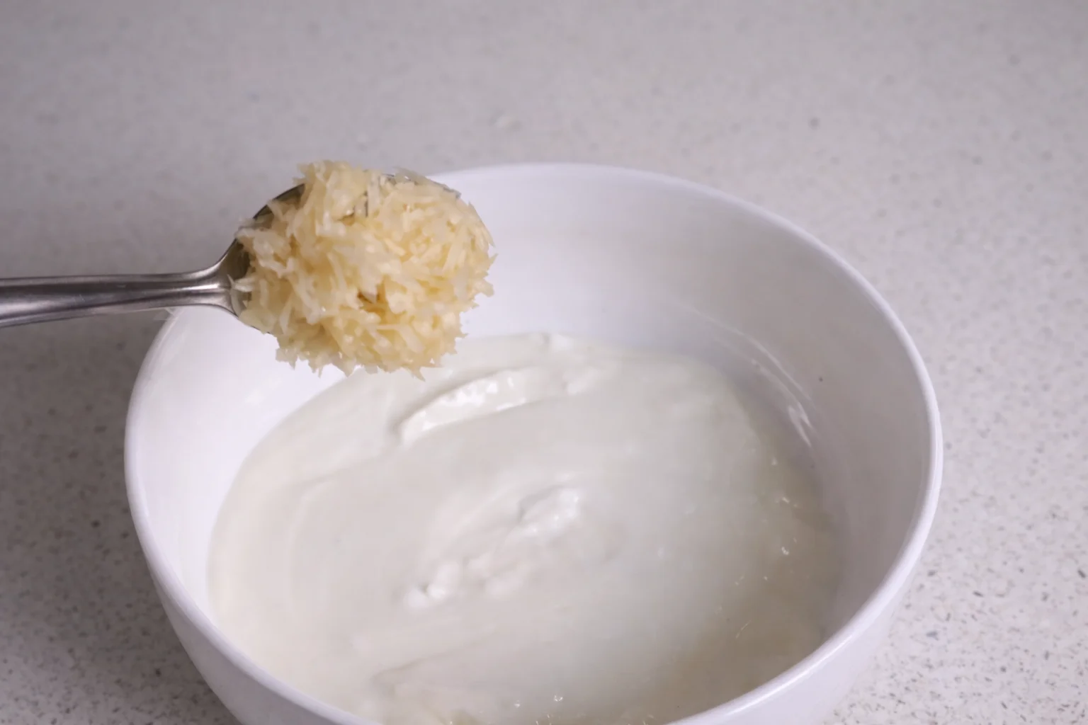 Creamy plain yogurt in a white bowl with freshly minced garlic on a spoon
