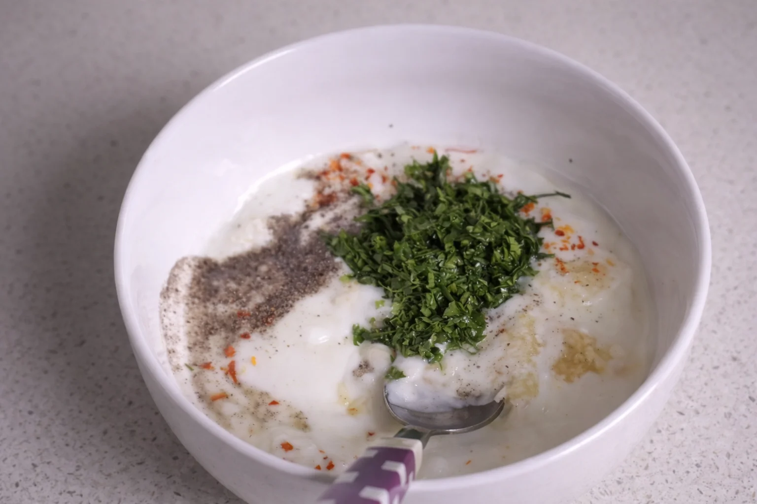 Chopped parsley added to garlic yogurt mixture with seasoning in a bowl