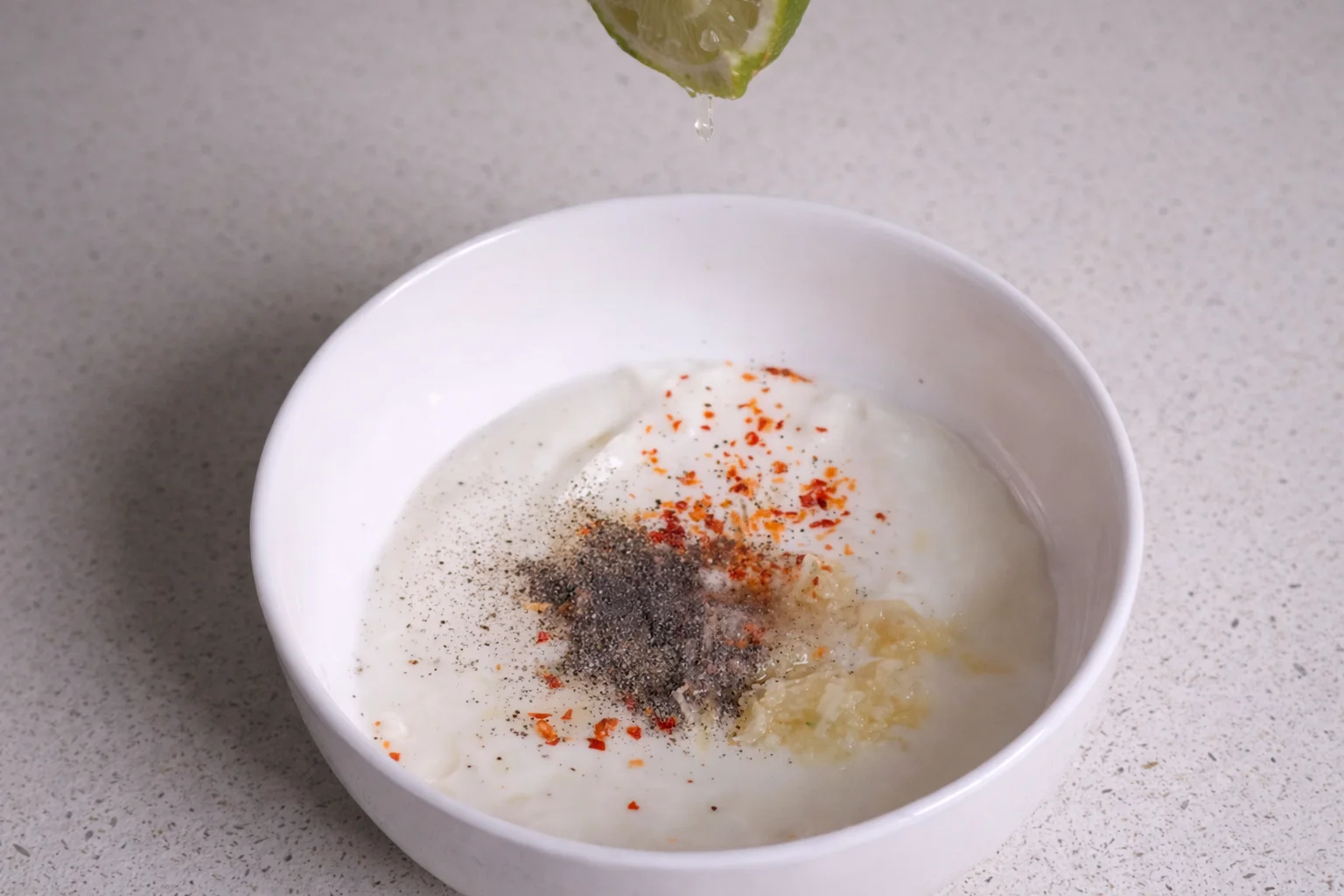 Garlic yogurt mixture with lemon juice, black pepper, and chili flakes being added