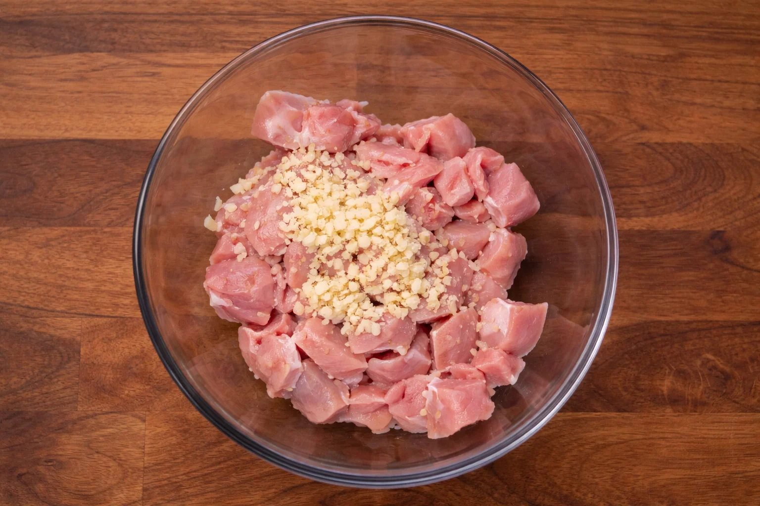 Raw chicken pieces mixed with garlic and seasoning in a bowl