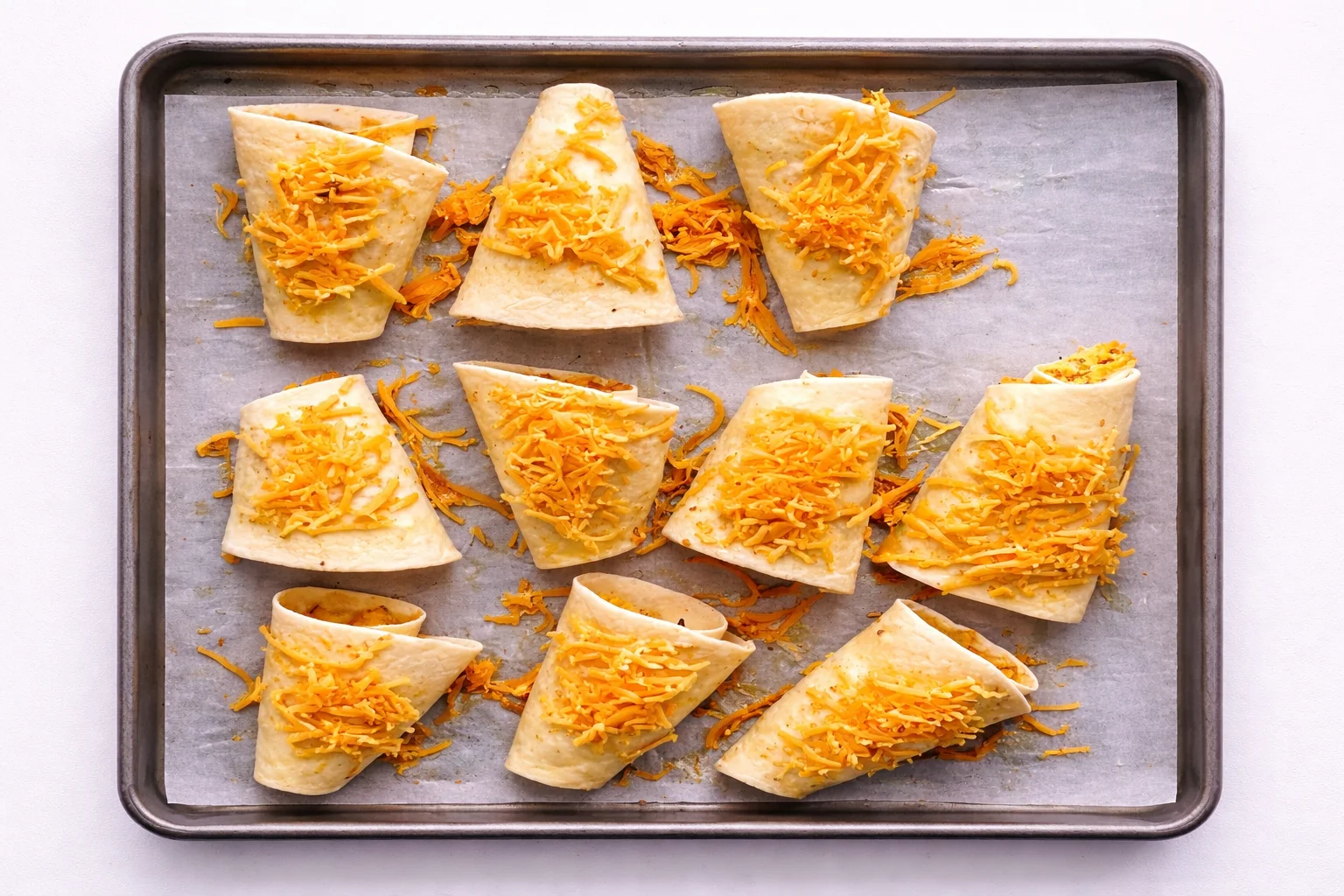 Unbaked buffalo chicken cones topped with shredded cheese on baking sheet