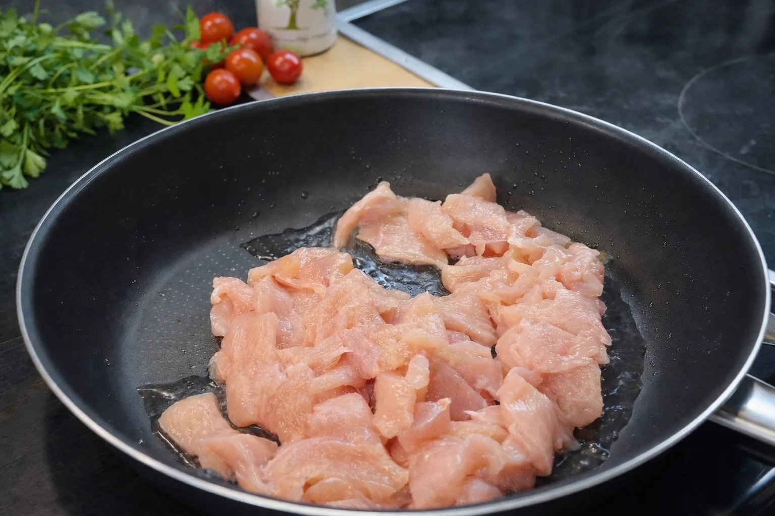 Raw sliced chicken cooking in a skillet with olive oil