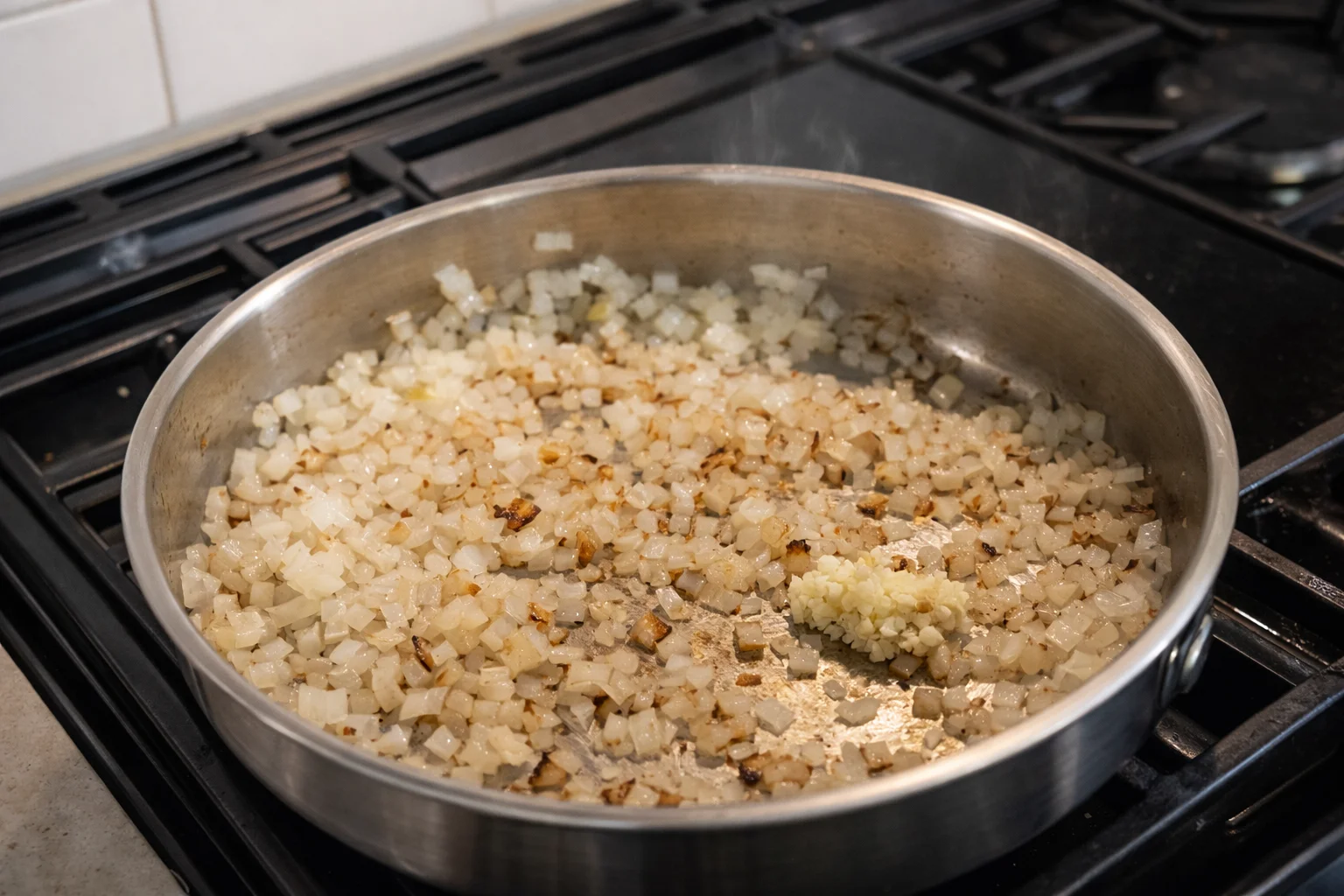 Finely diced onions sautéing with garlic in olive oil in a stainless steel skillet on a gas stovetop