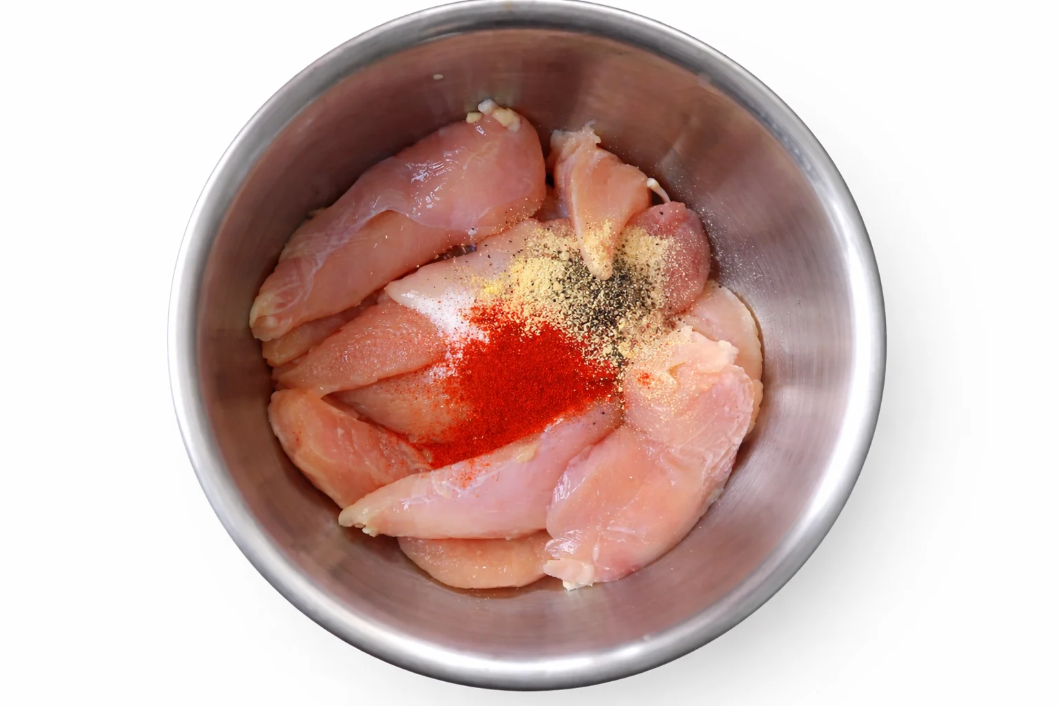 Chicken tenders with seasoning spices added on top before mixing