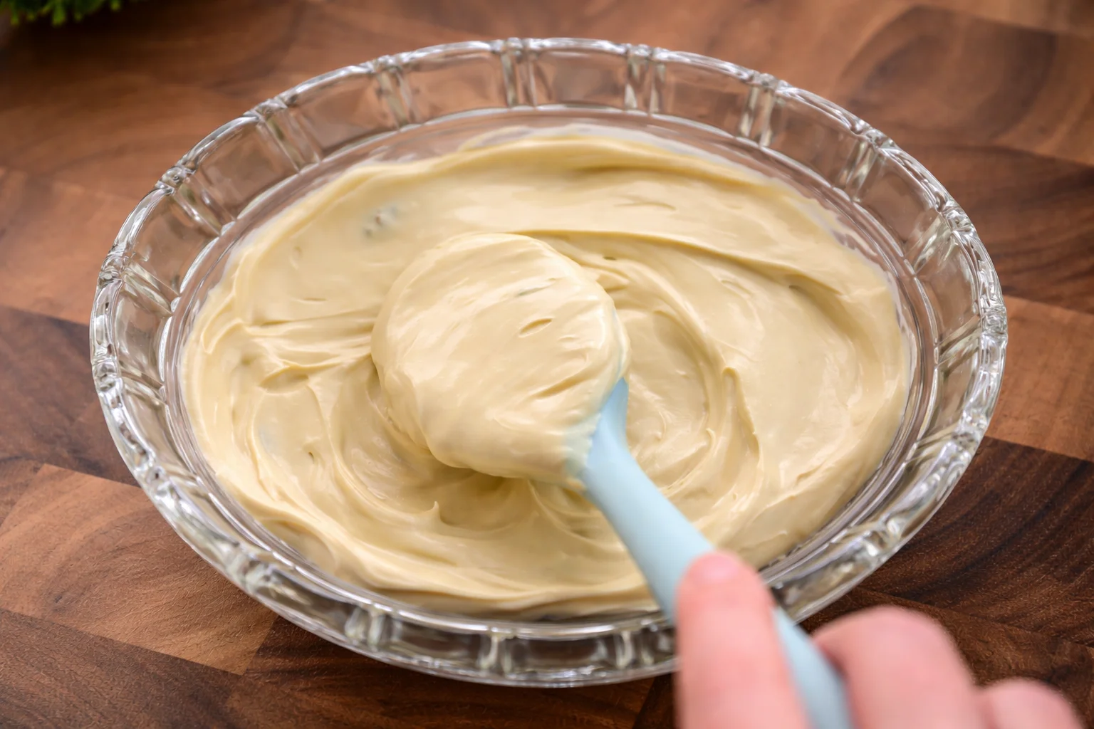 Creamy Biscoff mascarpone mixture being gently spread in a glass dish with a spatula

