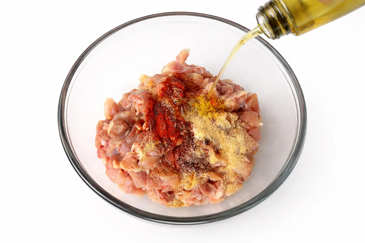 Raw diced chicken seasoned with paprika garlic powder salt black pepper and olive oil in a glass bowl for crispy chicken quesadillas