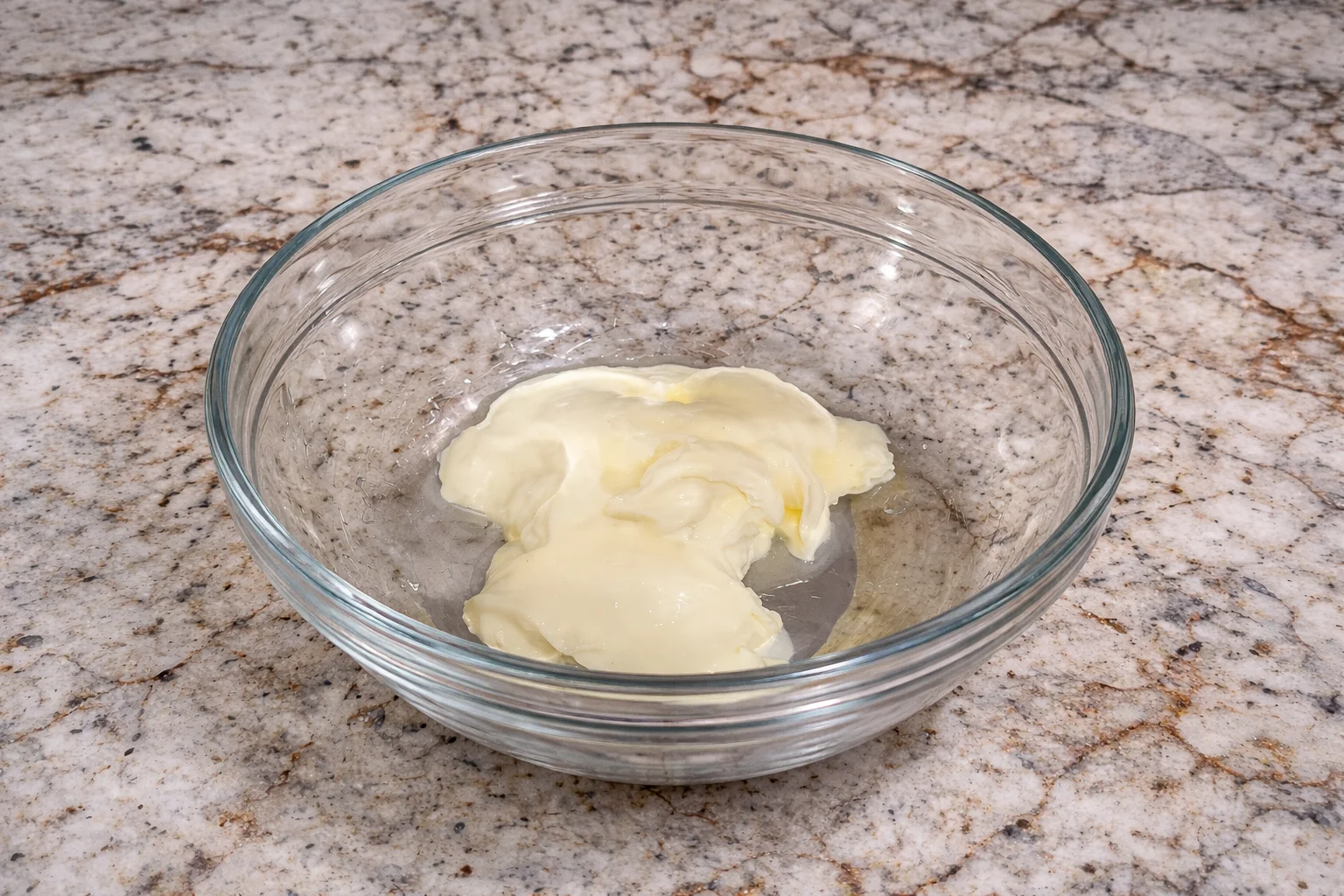 Full-fat mayonnaise added to a clear glass bowl as the base for homemade beef cone sauce on a marble countertop