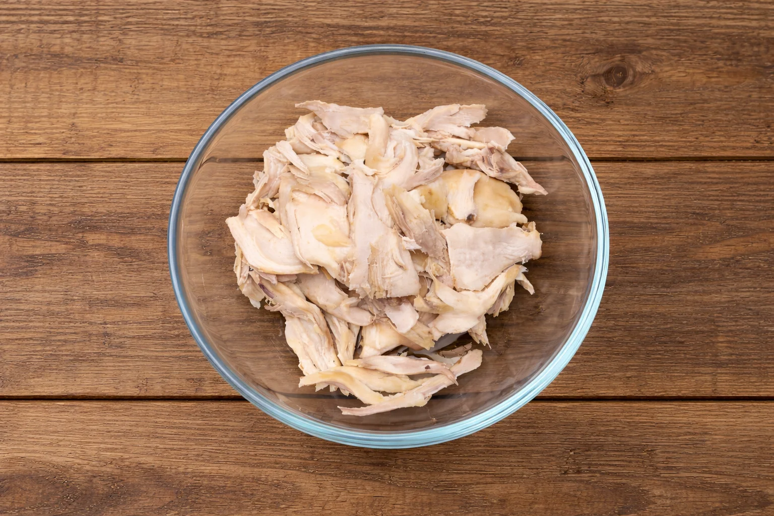 Shredded rotisserie chicken in a glass bowl ready for buffalo chicken dip