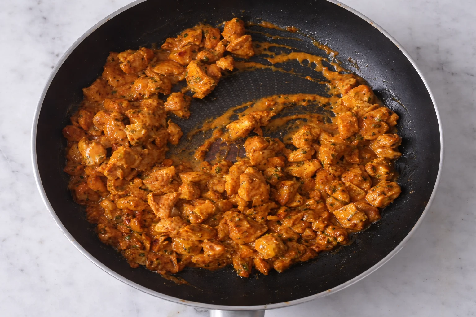 Seasoned chicken cooking in skillet with creamy spicy sauce thickening