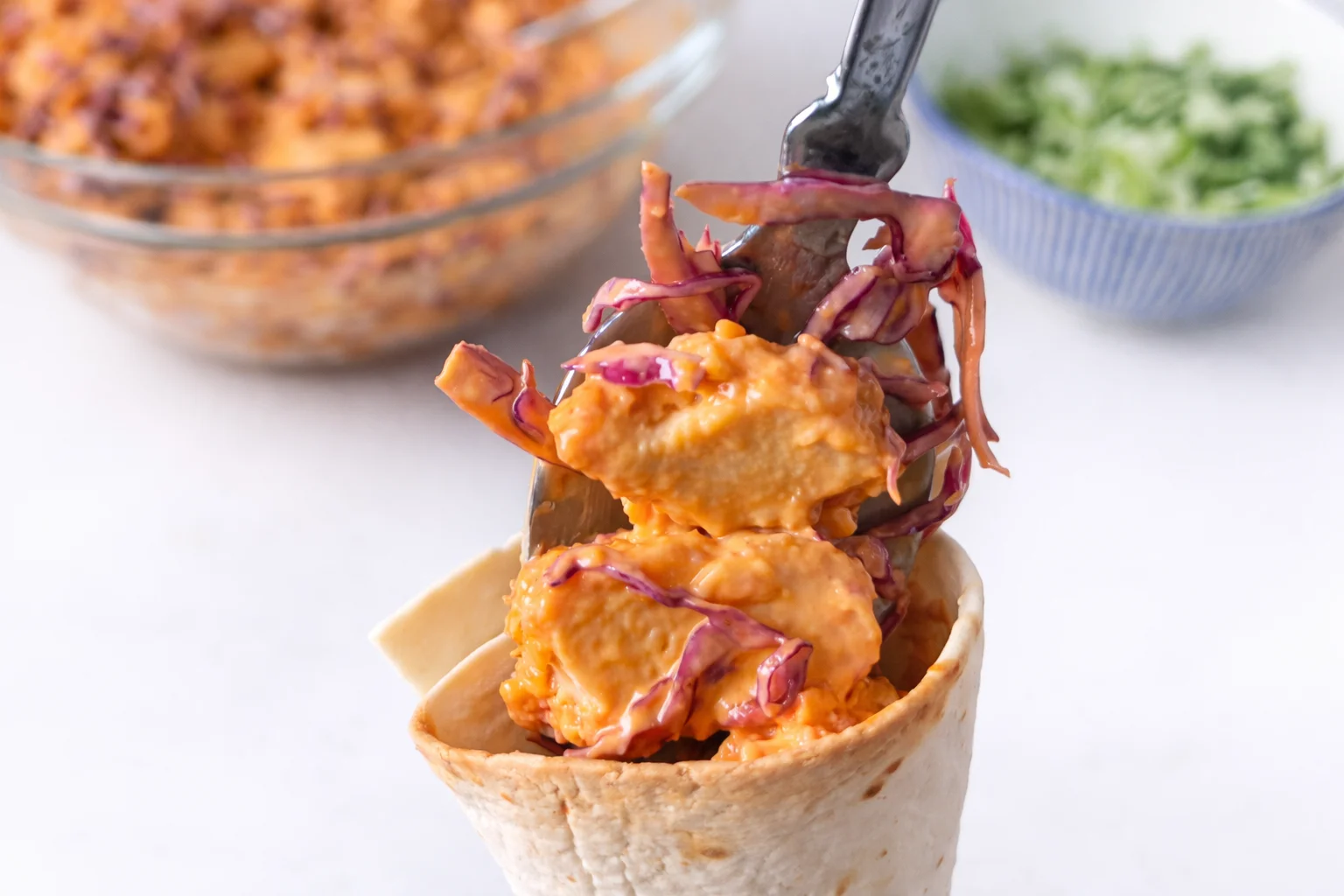 Creamy buffalo chicken filling spooned into a crispy tortilla cone ready to serve