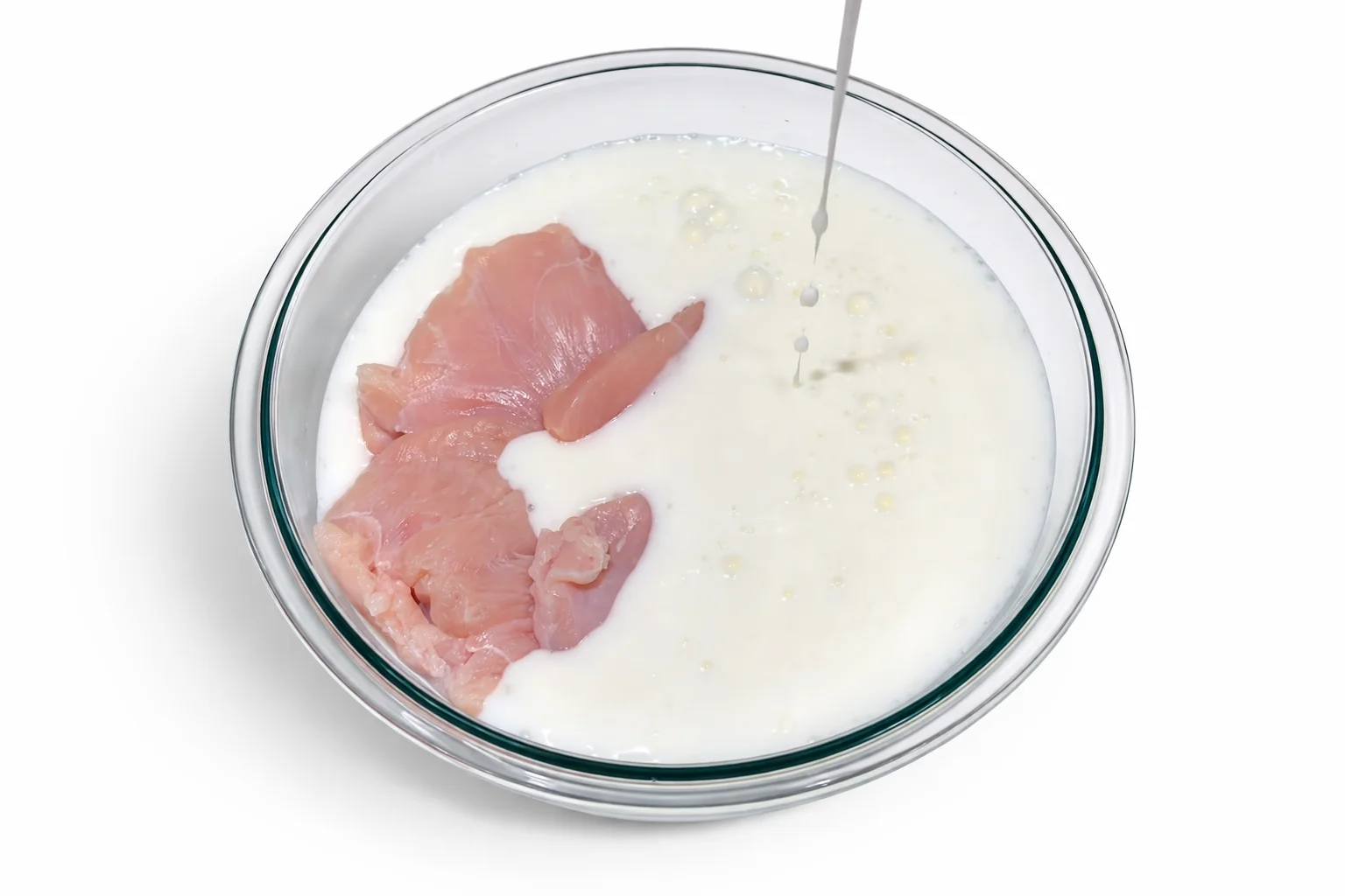 Chicken pieces soaking in buttermilk marinade in a glass bowl