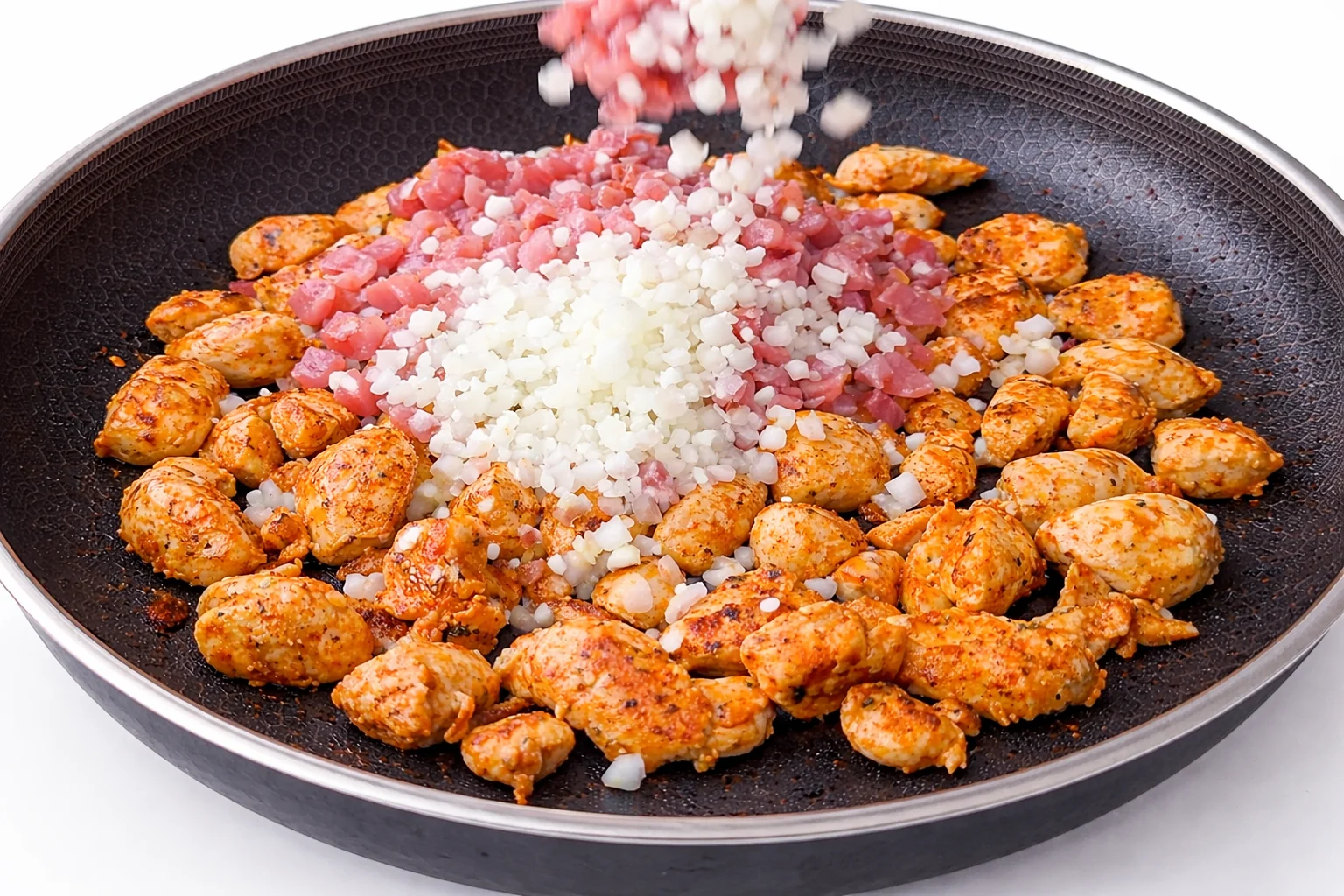 Diced onion and bacon cooking with seasoned chicken in skillet for creamy chicken and bacon rice