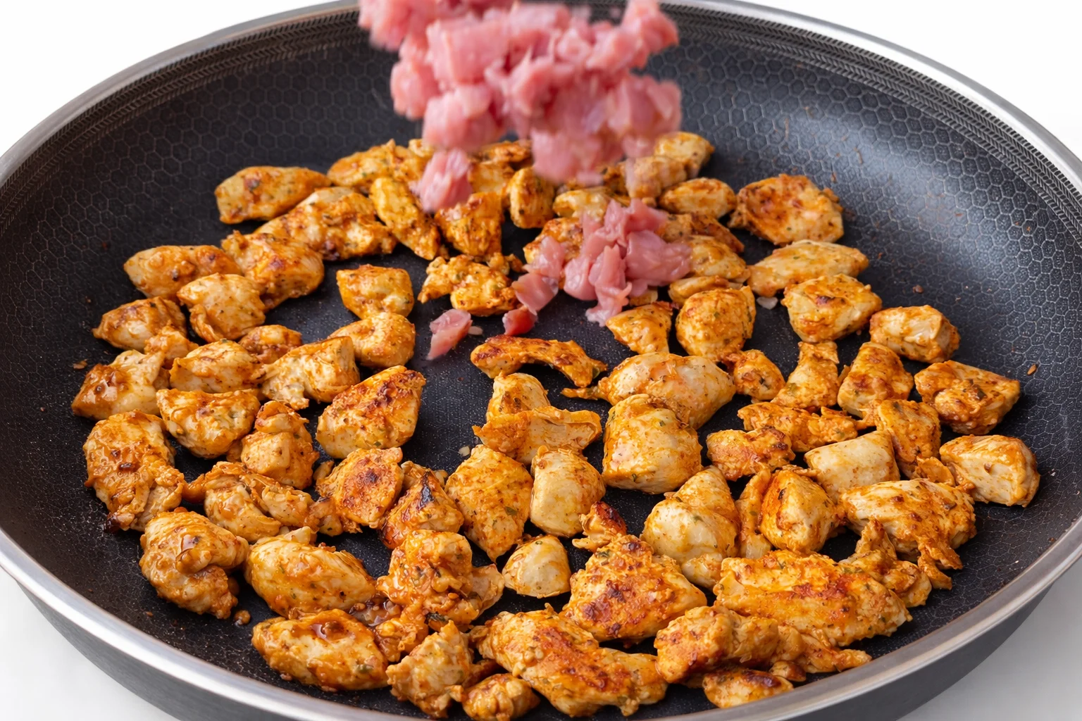 Seasoned chicken pieces browning in a nonstick skillet as diced bacon is added for creamy chicken and bacon rice