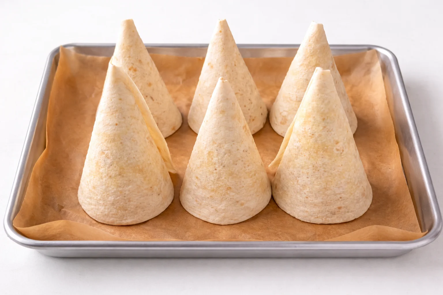 pizza cones recipe step 1 shaping flour tortillas into cone shapes on a parchment lined baking tray before baking