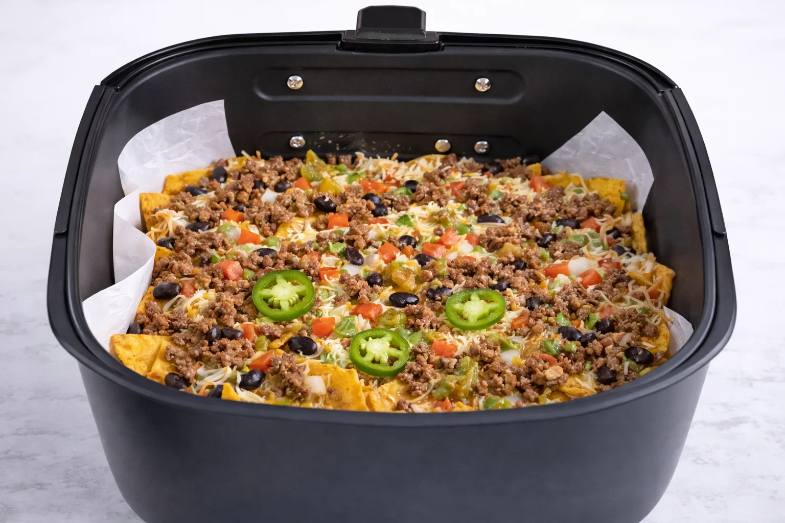 The nachos are now fully layered with chips beef beans cheese and toppings ready to melt together in the air fryer.