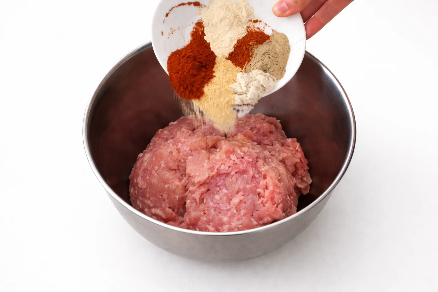 Paprika, garlic powder and seasonings being added to ground chicken in a mixing bowl for homemade oven baked chicken nuggets