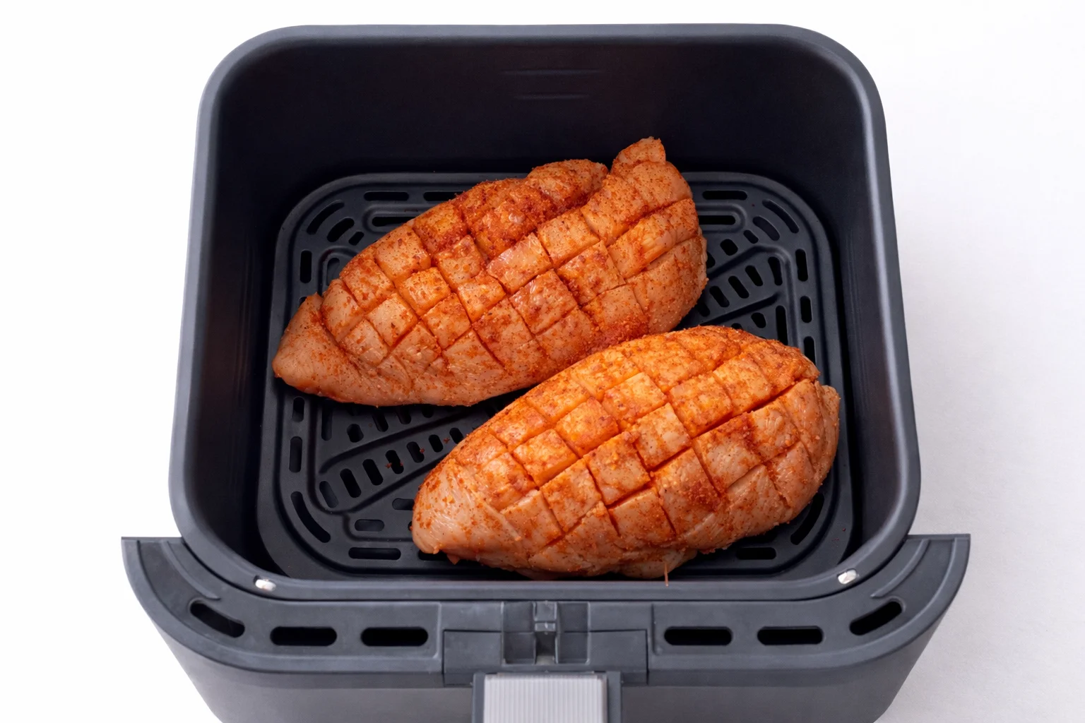 Chicken breast arranged in air fryer basket before cooking