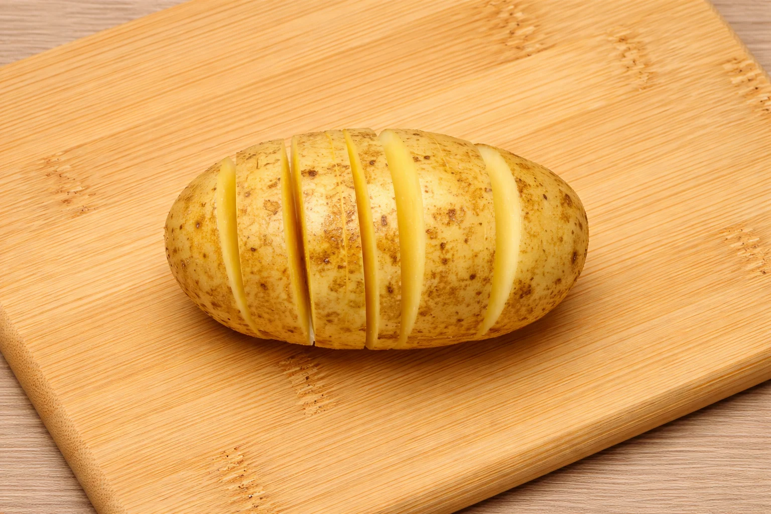 Hasselback potatoes sliced thinly on a cutting board before cooking