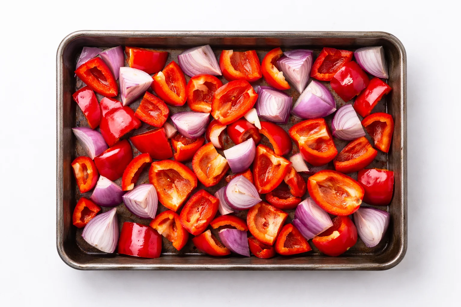 chopped red peppers and red onion pieces arranged on a baking tray before roasting