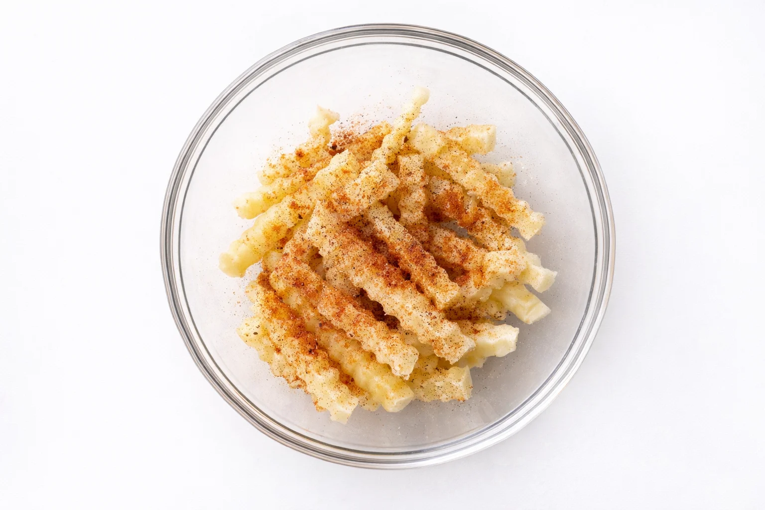 seasoning frozen french fries with paprika garlic powder salt and pepper in a glass bowl